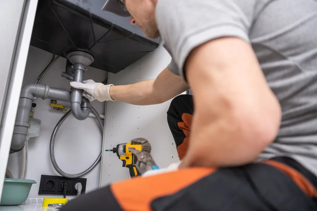 A plumber from Drain Pros Venture working on the pipes underneath a kitchen sink.